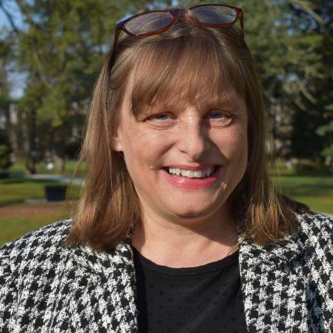 Shay Humphrey ’91, Vassar’s first general counsel wearing a black shirt and black and white jacket, standing outside with trees in the background 