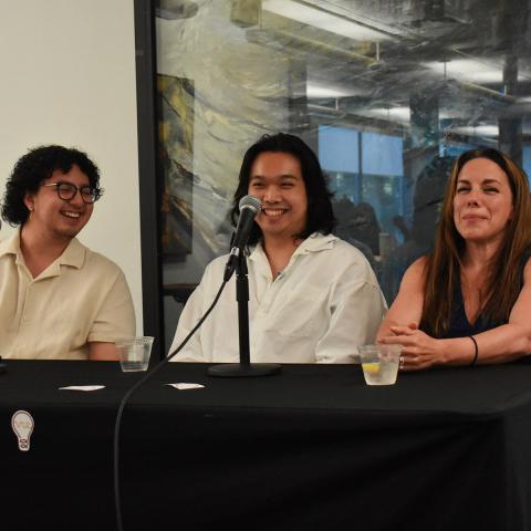 Three people sitting at a table smiling with microphones in front of them