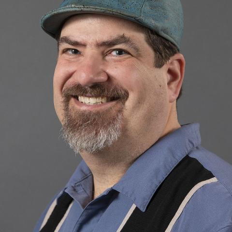 Man in a blue shirt and derby hat smiling