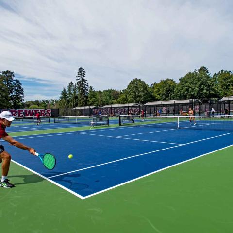 corner view of two tennis courts with players on each end