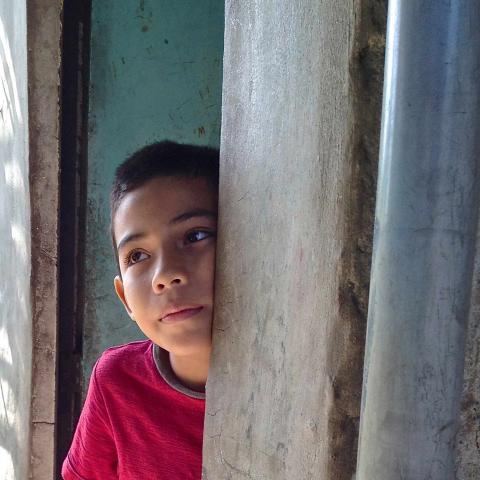 An image of a you boy peering out of a doorway from Amy Kaslow's exhibit, "LifeI After War: Disturbed".