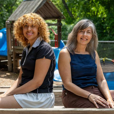 Student and professor seated facing the camera with a playground in the background.