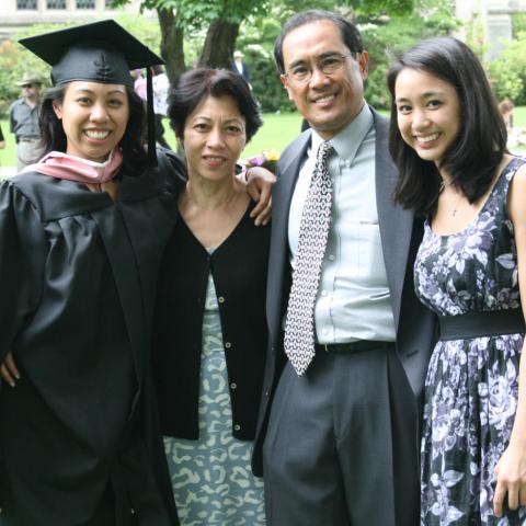 Four people smiling at the camera. One of the people is dressed in graduation robes.