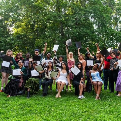 A large group of students who are standing in two lines holding up a diploma and smiling. 