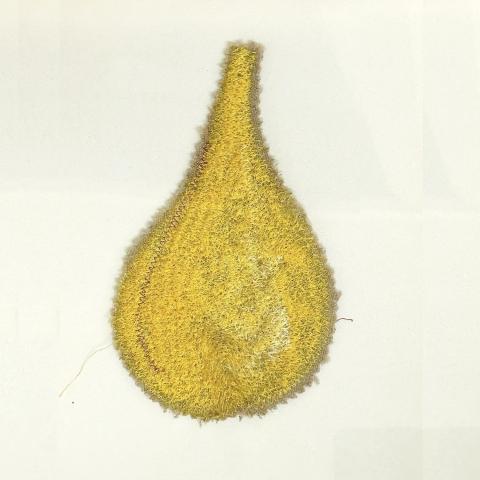 A yellow fuzzy teardrop shaped artwork on a white wall.