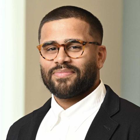 A portrait of Stephen Andrade, a person with short black hair and beard, glasses, and a dark suit coat.