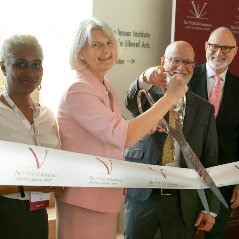 Four of smiling people cutting a ribbon together.