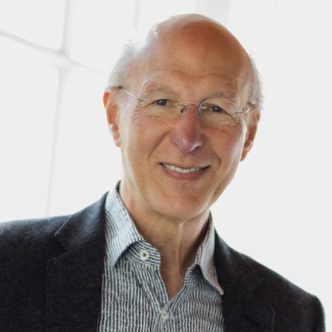 A photograph of Paul Foxman, author of The Worried Child, is facing the camera and wearing wire-rimmed glasses and a black blazer over a grey and white striped shirt.     