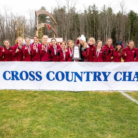 Large group of smiling athletes standing behind a banner that reads: cross country champions.