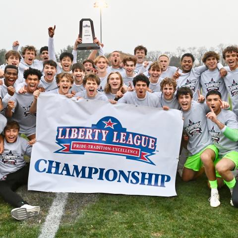 A group of people celebrating behind a banner that reads: Liberty League Championship, Pride, Tradition, Excellence.