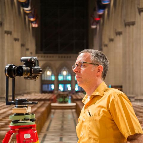 Andrew Tallon wearing a yellow shirt inside the Washington National Cathedral with a camera on a tripod. 