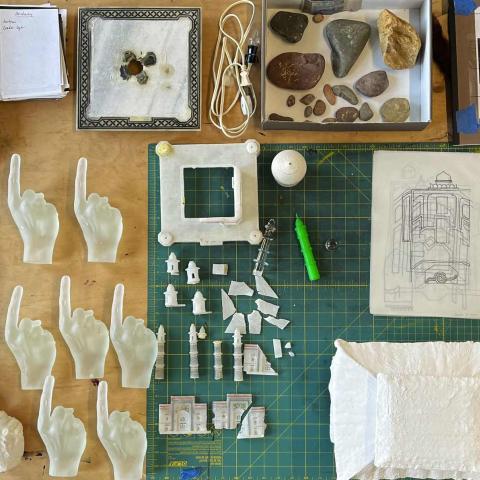 A wooden artist’s desk covered with objects: plaster casts of hands pointing a finger, pencils, sketches, a drafting board, etc.