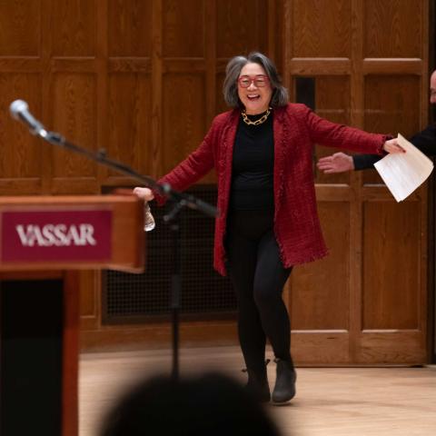 Smiling person with arms held out walks onto a stage.