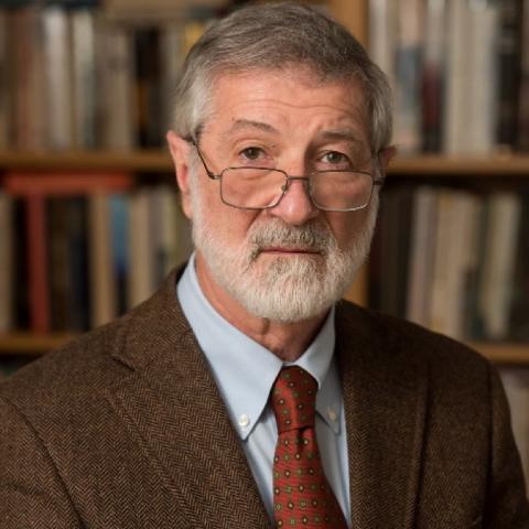 Dr. Ira Helfand, wearing eyeglasses, a light blue shirt, brown tweed jacket, red patterned tie with a bookcase in the background.