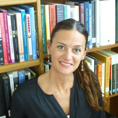 A portrait photo of Natalia Milanesio  posing in front of a bookshelf.