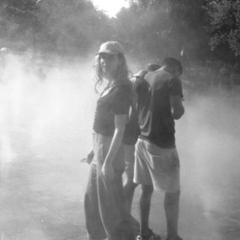 Black and white image of two people standing outside, back to back, with fog all around them.