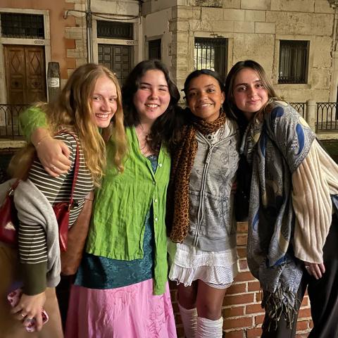 Picture of four people standing outside in a city with their arms around each other smiling.