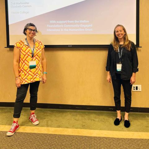 Two smiling people standing in front of a projected slide presentation on a wall.