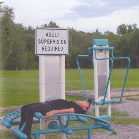 Photo of boy lying on outdoor exercise equipment below sign reading "Adult Supervision Required".