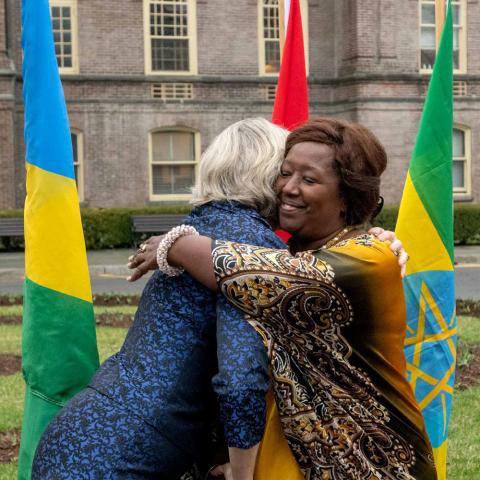 President Elizabeth Bradley and UGHE Vice Chancellor Agnes Binagwaho embracing in front of some flags with main building in the background.