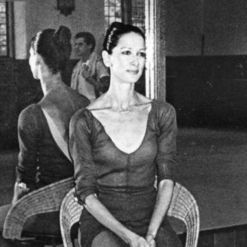 Jeanne Czula, dance teacher seated on a stool in a dance studio.