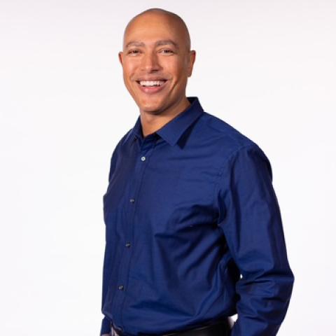 Portrait photo of Torrey Maldonado standing and smiling with his hands in his pockets.