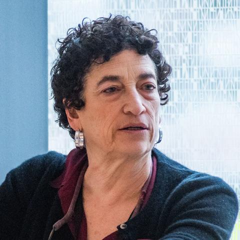 Person speaking to an an audeince in front of a window with trees in the background.