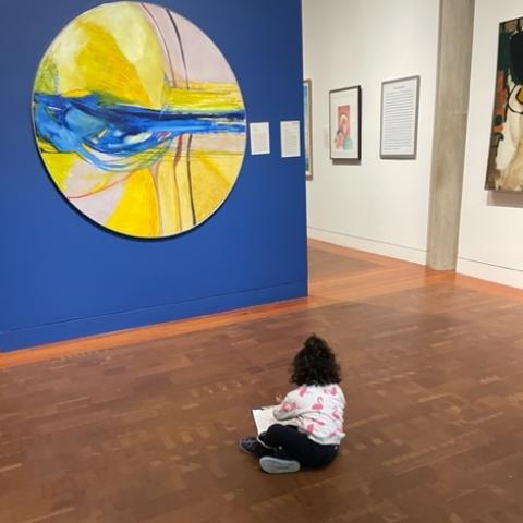 Child seated on the floor in a museum gallery in front of a colorful abstract painting