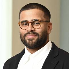 A portrait of Stephen Andrade, a person with short black hair and beard, glasses, and a dark suit coat.