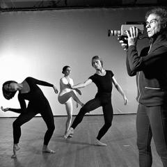 A grayscale photo showing three people performing dance moves while a fourth person films the scene with a video camera.