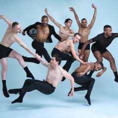 A number of people perform dance moves, posing against a light blue background.